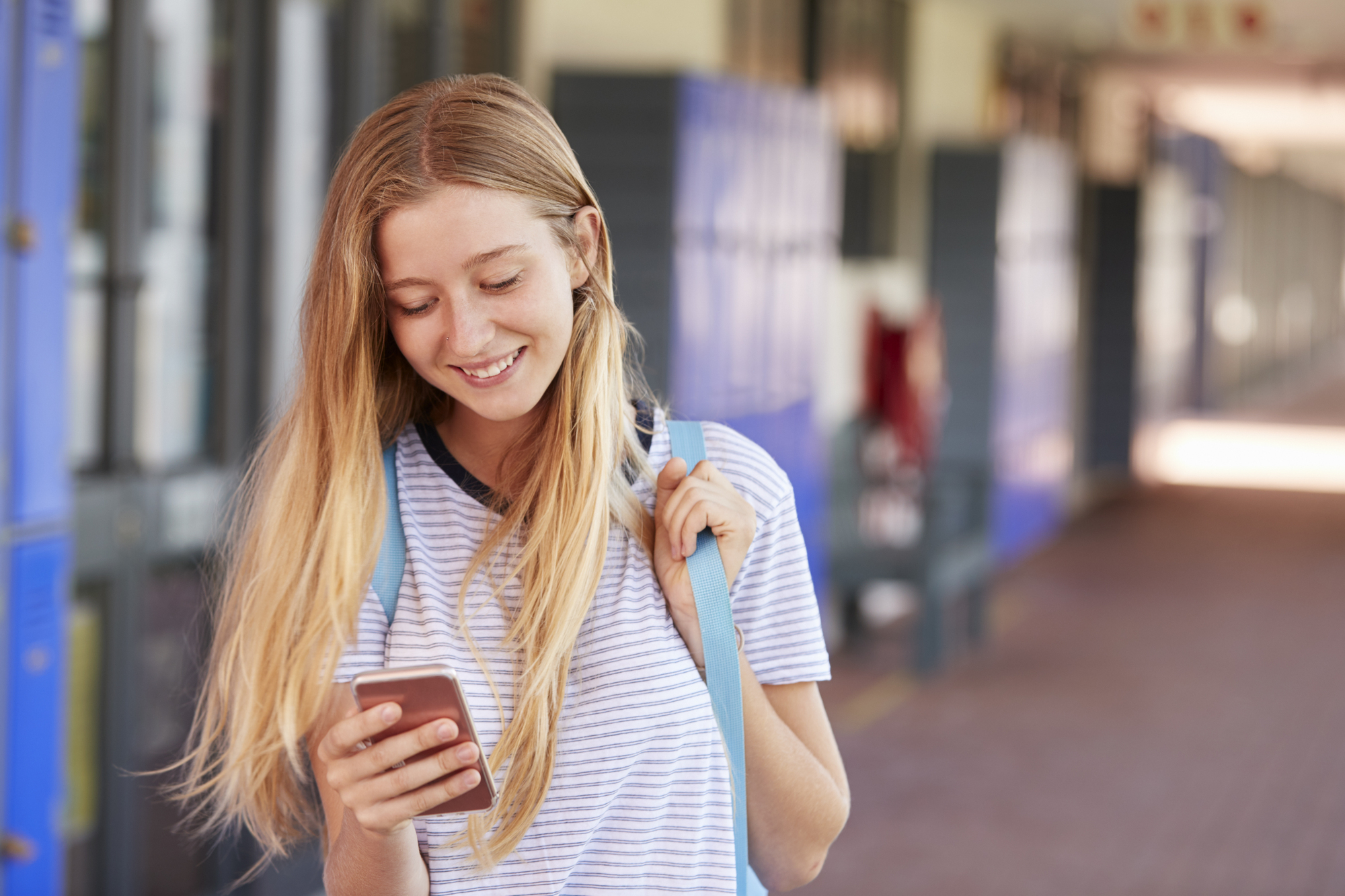 happy-teenage-girl-using-smartphone-in-school-corr-PJT7HVC